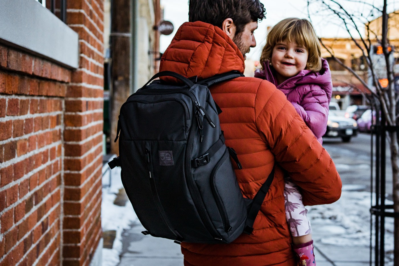 Dad wearing the Ready 22L EDC Diaper Backpack on a city sidewalk while holding his child