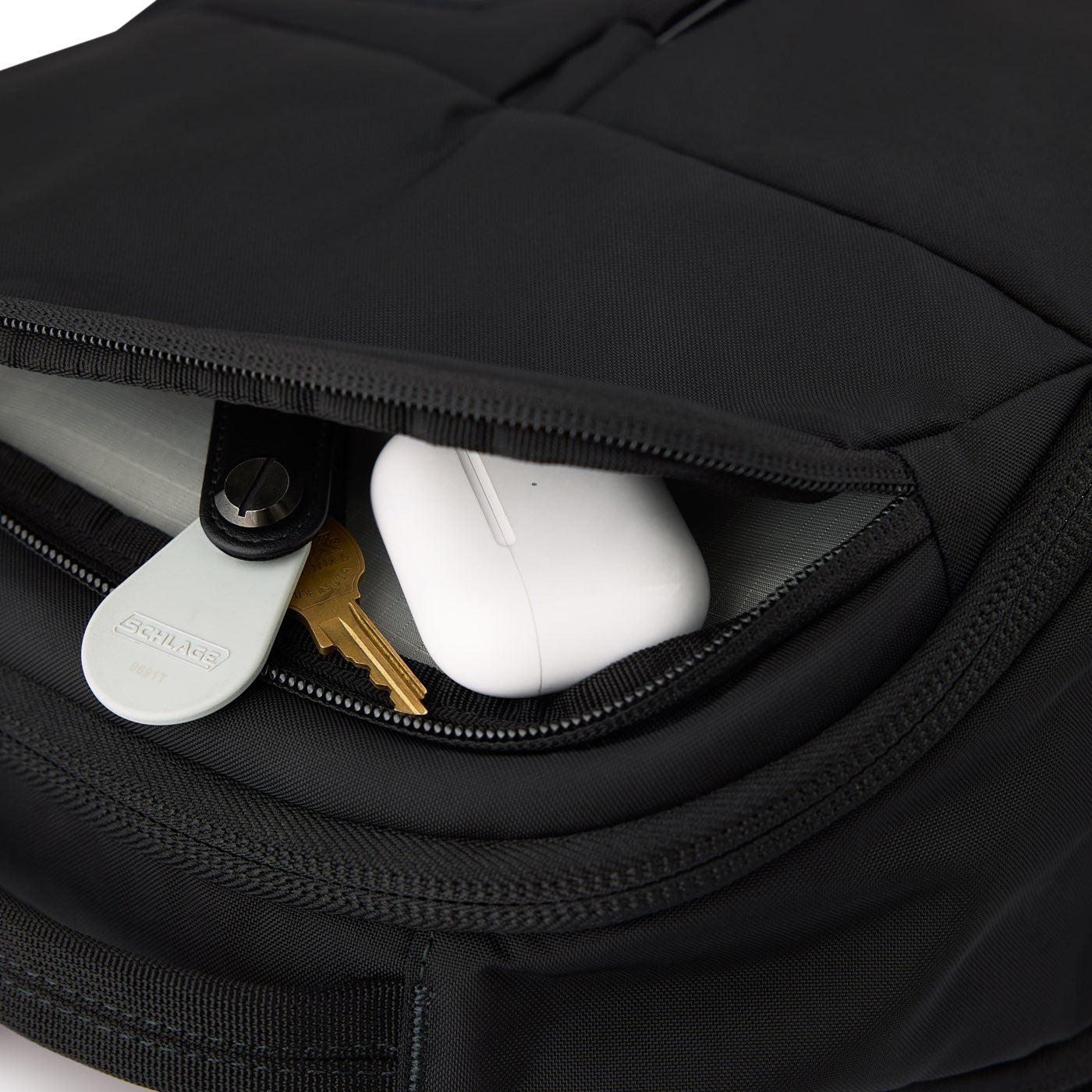Close-up of the Black recycled CORDURA shell and top zip pocket, with keys and AirPods inside